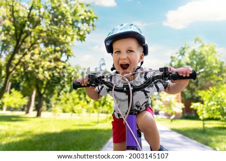 Portrait little cute adorable caucasian toddler boy in safety helmet enjoy having fun riding exercise bike in city park road yard garden forest. Child first bike. Kid outdoors sport summer activities