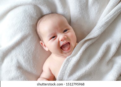 Portrait of little cute baby 1-2 months old lying on white blanket laughing and smiling at camera. Healthy newborn mixed race Asian-German infant.