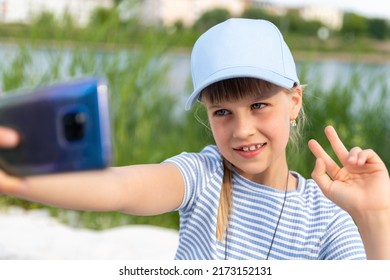 Portrait of little cute beautiful blond caucasian girl wear blue cap enjoy having fun taking selfie photo phone camera resting at beach outdoors on summer day. Children blogging and video streaming
