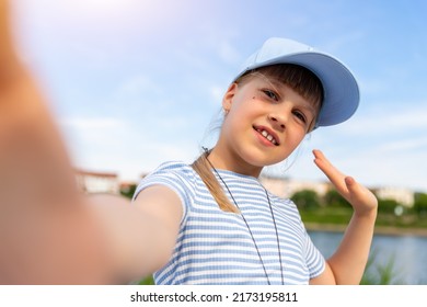 Portrait of little cute beautiful blond caucasian girl wear blue cap enjoy having fun taking selfie photo phone camera resting at beach outdoors on summer day. Children blogging and video streaming
