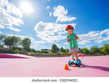 Portrait Of The Little Cute Small Boy On The Kick Scooter Ride Around Orange Cones On The Skatepark With Color Surface In Helmet