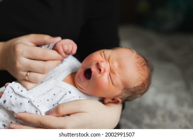 a portrait of a little cute sweet adorable caucasian newborn infant baby is yawning in his mother's hands. Tenderness and love of maternity and parenthood. Childrens' sleep concept. 
