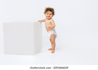 Portrait of little cute toddler boy, baby in diaper cheerfully standing near cube and smiling isolated over white studio background. Concept of childhood, motherhood, life, birth. Copy space for ad
