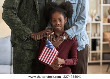 Portrait of little girl with american flag looking at camera standing in the room with her family