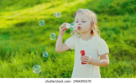 Portrait Of Little Girl Child Blowing Soap Bubbles In Summer Park