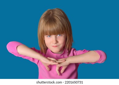 Portrait Of A Little Girl Dressed In A Pink Sweater On A Blue Background. The Child Poses For The Camera With A Sly Expression.