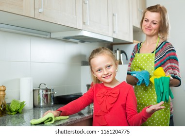 Portrait Of Little Girl Helping Her Joyful Mom Tidy Up At Home Kitchen
