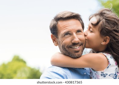 Portrait of a little girl kissing her dad on cheek. Pretty girl giving a kiss to her father outdoor. Loving child embrace and kissing her father.