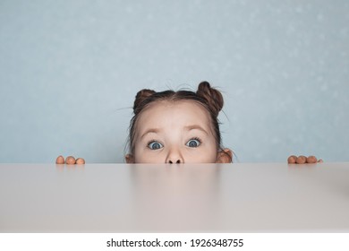 Portrait Of Little Girl Looking From Under The Table. High Quality Photo