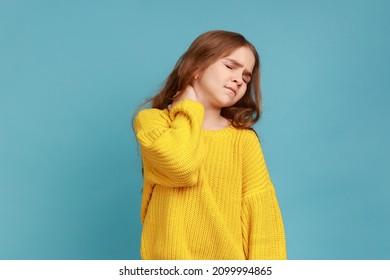 Portrait Of Little Girl Massaging Painful Back, Feel Discomfort In Neck, Child Sedentary Lifestyle, Wearing Yellow Casual Style Sweater. Indoor Studio Shot Isolated On Blue Background.