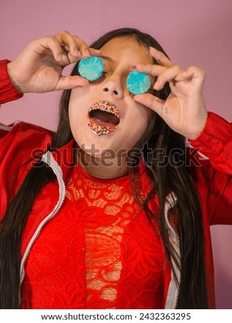 portrait of a little girl playing with coloured biscuits while covering her eyes with them