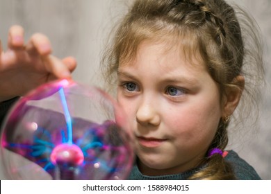 Portrait of a little girl playing with a plasma ball. The child touches the surface of the lamp, causing lightning. Selective focus.