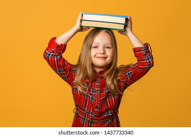 Portrait of a little girl schoolgirl on a yellow background. The child holds books on his head. The concept of education and school. - Shutterstock ID 1437733340