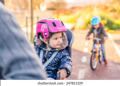 Portrait of little girl with security helmet on the head sitting in bike seat and her brother with bicycle on the background. Safe and child protection concept
