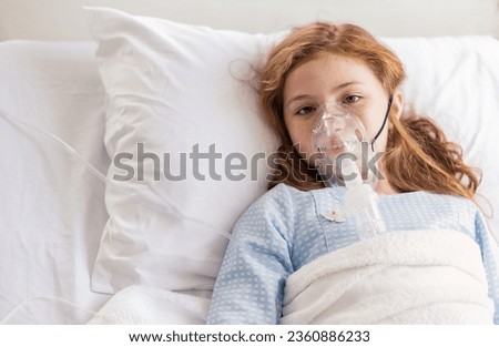 Portrait of little girl suffering from pneumonia lying in hospital bed with oxygen mask. Teenage kid patient with asphyxia breath in oxygen mask sleeping in bed at ward. Oxygen face mask of cute girl
