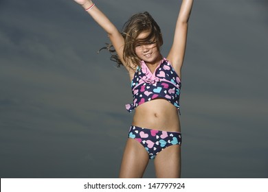 Portrait of a little girl in swimwear raising hands on a beach