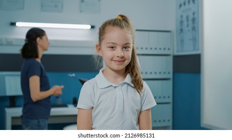 Portrait of little girl waiting to do medical examination with doctor, sitting on bed in cabinet. Child in office preparing to talk to pediatrician at checkup visit appointment. Health care - Powered by Shutterstock