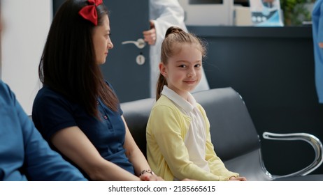 Portrait Of Little Girl Waiting With Mother At Hospital Reception Lobby, Having Medical Consultation Appointment. Small Child Sitting In Waiting Room Area, Healthcare Examination.