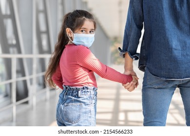 Portrait Of Little Girl Wearing Medical Mask While Walking With Father At Airport, Small Female Child Holding Dad's Hand And Turning At Camera, Traveling With Parent During Coronavirus Pandemic