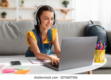 Portrait of little girl in wireless headset using laptop, studying online at home, interested happy student typing on keyboard looking at pc screen, watching webinar, online course, doing homework - Shutterstock ID 2074607506