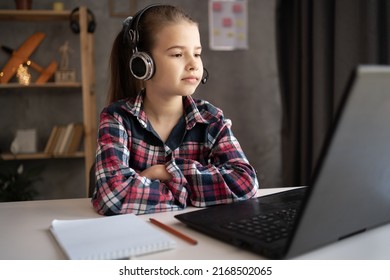 Portrait Of Little Girl In Wireless Headset Using Laptop, Studying Online At Home, Interested Happy Student, E-learning, Distance Education At Home, Student Dreaming And Look To Window