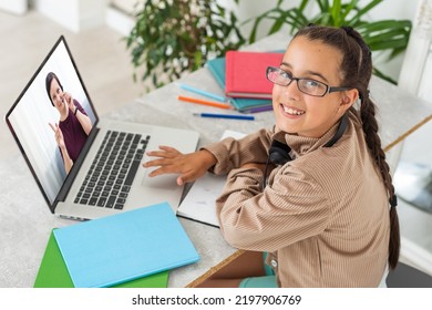 Portrait Of Little Girl In Wireless Headset Using Laptop, Studying Online At Home, Interested Happy Student Typing On Keyboard Looking At Pc Screen, Watching Webinar, Online Course, Doing Homework.