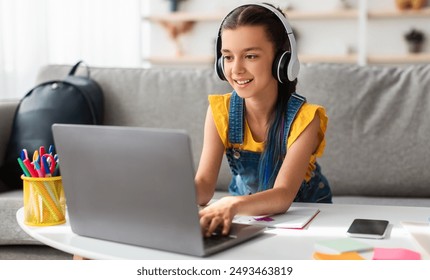 Portrait of little girl in wireless headset using laptop, studying online at home, interested happy student typing on keyboard looking at pc screen, watching webinar, online course, doing homework - Powered by Shutterstock