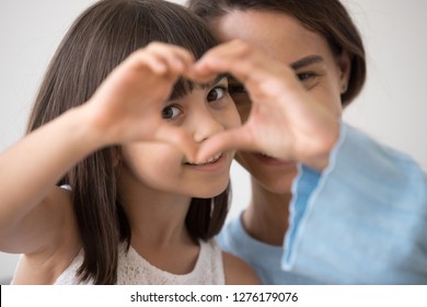 Portrait of little happy girl and mother join hands forming heart shape as concept of giving love, child mum connection unity, cute kid daughter and mom bonding looking at camera, child care adoption - Shutterstock ID 1276179076