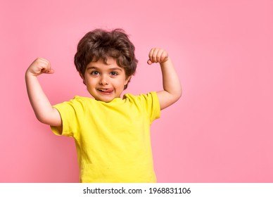 Porträt eines kleinen Jungen einzeln auf rosafarbenem Hintergrund mit Zunge. Seltsamer kleiner Strom Superheldenkind mit Muskeln. Stärke, Selbstvertrauen oder Schutz vor Mobbing. Kindergarten oder Schulkind