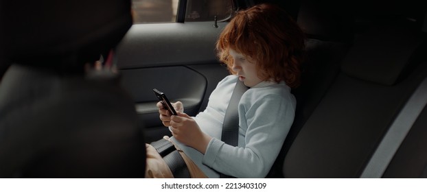 Portrait Of Little Kid Boy Using His Phone On The Back Seat While Taking A Ride To School. Shot With 2x Anamorphic Lens