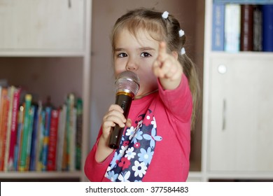 Portrait Of Little Kid Singing Into Microphone And Pointing To Somebody At Home, Entertainment And Education Concept, Indoor