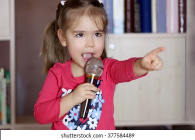 Portrait Of Little Kid Singing Into Microphone And Pointing To Somebody At Home, Entertainment And Education Concept, Indoor