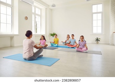 Portrait of a little kids girls sitting on the floor with their teacher and practicing yoga sitting in gym in Lotus pose with closed eyes. Children sport and active lifestyle concept. - Powered by Shutterstock