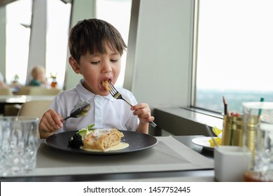 Portrait Of Little Mixed Race Asian-German Boy Eating Apple Strudel With Spoon And Fork At Restaurant.kid With Sweet Food