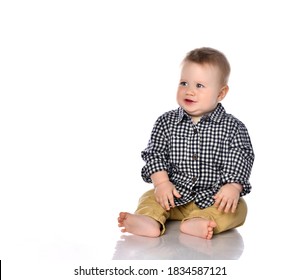 Portrait of a little one-year-old boy on a white background. The boy sits in a shirt and shorts with tears in his eyes. The boy is capricious because his toy was taken away. 