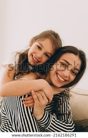 Portrait of little preteen girl hugging her elder sister of 20s in striped clothes, putting hands around neck, showing her love and affection. Family, relatives, siblings concept. Happy childhood