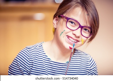 Portrait of a little pre-teen student girl painting at home.  Girl with teeth braces and glasses.