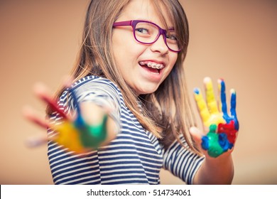 Portrait of a little pre-teen student girl showing painted hands. Girl with teeth braces and glasses. 