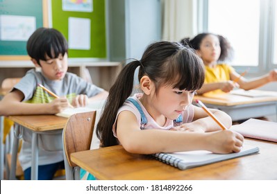 Portrait of little pupil writing at desk in classroom at the elementary school. Student girl doing test in primary school. Children writing notes in classroom. Education knowledge concept