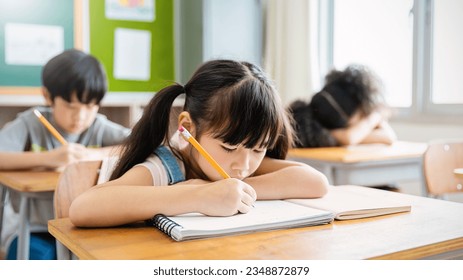 Portrait of little pupil writing at desk in classroom at the elementary school. Student girl study doing test in primary school. Children writing notes in classroom. Education knowledge (blur) - Powered by Shutterstock