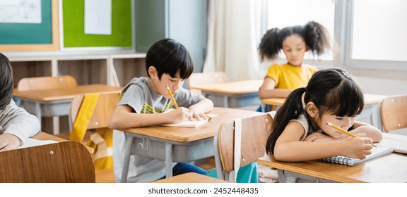 Portrait of little pupil writing at desk in classroom at the elementary school. Student girl study doing test in primary school. Children writing notes in classroom. Education knowledge concept - Powered by Shutterstock