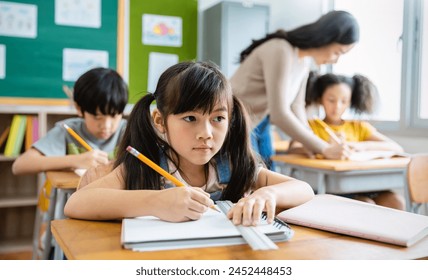 Portrait of little pupil writing at desk in classroom at the elementary school. Student girl study doing test in primary school. Children writing notes in classroom. Education knowledge concept - Powered by Shutterstock