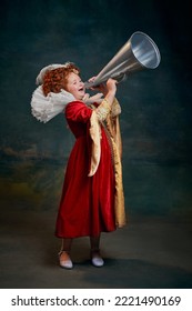 Portrait Of Little Red-headed Girl, Child In Costume Of Royal Person Shouting In Megaphone Isolated On Dark Green Background. Concept Of Historical Remake, Comparison Of Eras, Medieval Fashion, Queen