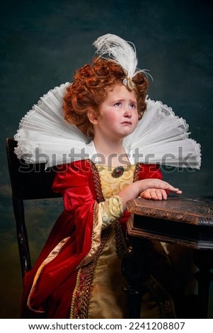 Portrait of little red-headed girl, child in costume of royal person crying isolated over dark green background. Concept of historical remake, comparison of eras, medieval fashion, emotions, queen