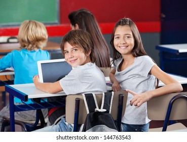 Portrait of little schoolchildren with digital tablet sitting at desk in classroom