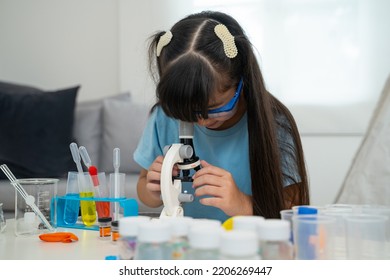 Portrait Of Little Scientist In Protective Glasses Playing With Microscope In Living Room 