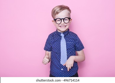 Portrait of a little smiling boy in a funny glasses and tie. School. Preschool. Fashion. Studio portrait over pink background