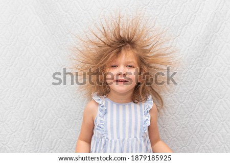 Portrait of a little smiling girl with electrified hair on a white background.
Electricity power concept.