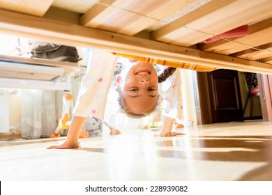 Portrait Of Little Smiling Girl Looking Under Bed