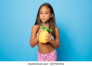 portrait of a little smiling girl in a swimsuit holding a pineapple on a blue background. Travel concept